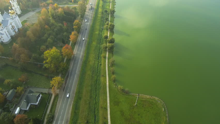 Aerial view from Drone: Road with a car along the autumn trees and green lake.