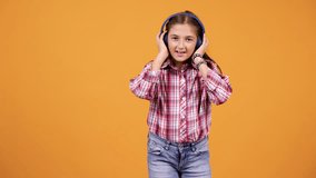 Happy smiling girl jumping while listening music isolated over yellow orange background in studio
