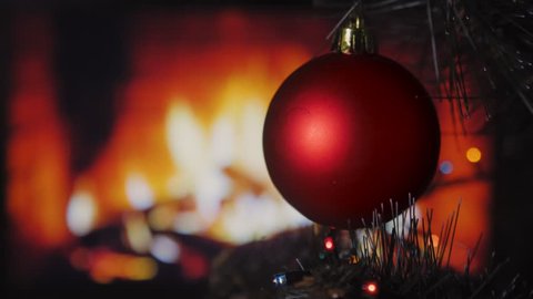 Single red holiday ornament hanging on tree with glowing fireplace in background. 4k