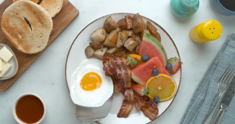 Adding a fried egg with a spatula to a breakfast plate with fruit, bacon and potatoes, ready to serve. Close up to Medium on 4k phantom flex.