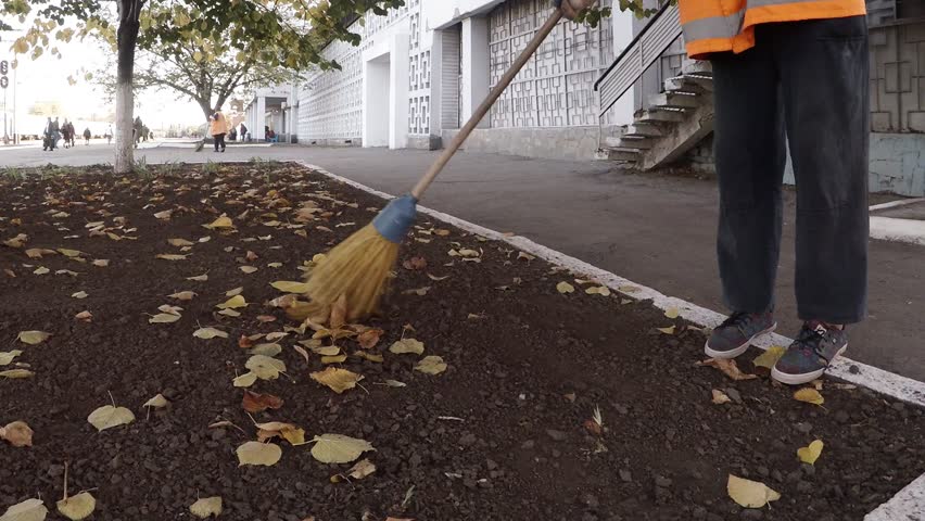 Woman janitor cleaning park from leaves in autumn, most hard and low-paid job