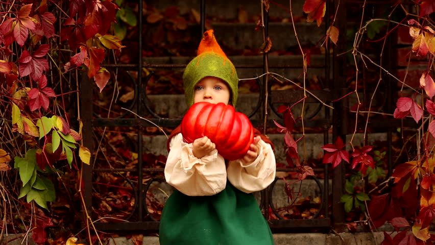Cute girl in a gnome costume holds a pumpkin for Halloween