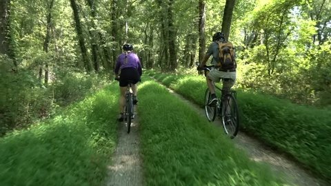 Mature daughter bikes next to her elderly father on the forested C&O Canal, a National Park near Harpers Ferry, West Virginia.