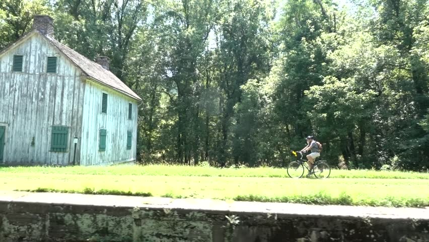 Elderly man cycles past an old white wooden building on the C&O Canal National Historic Park near Harpers Ferry, West Virginia.