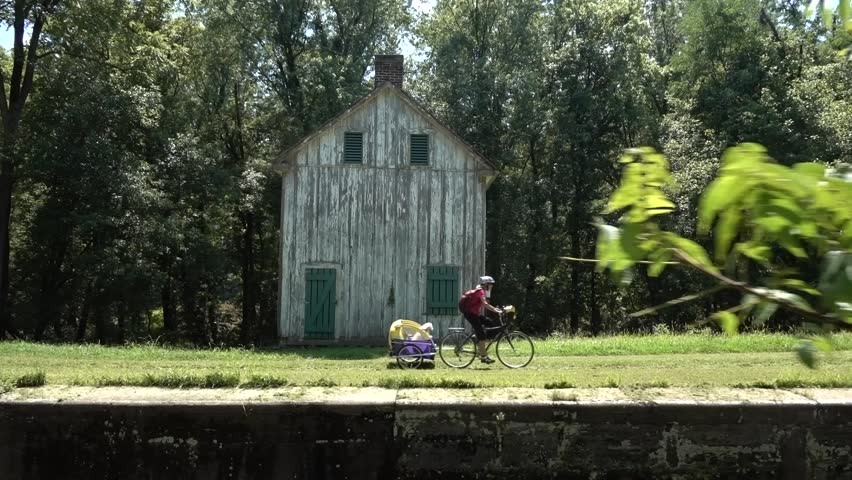 Mature woman bikes past an old building on the C&O Canal National Historic Park near Harpers Ferry, West Virginia.