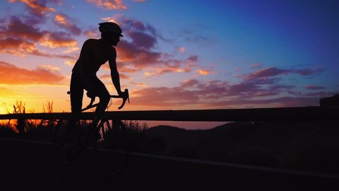 Silhouette of a man riding a Bicycle at sunset on a mountain road side view. Slow motion steadicam