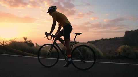 A young sports man riding a bike on a mountain serpentine in a yellow t-shirt helmet and sports equipment rear view . Slow motion steadicam