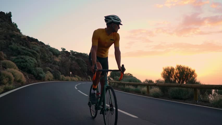 A young sports man rides a Bicycle on a mountain serpentine and looks at the camera in a yellow t-shirt and sports equipment. Slow motion steadicam | Shutterstock HD Video #1018822315