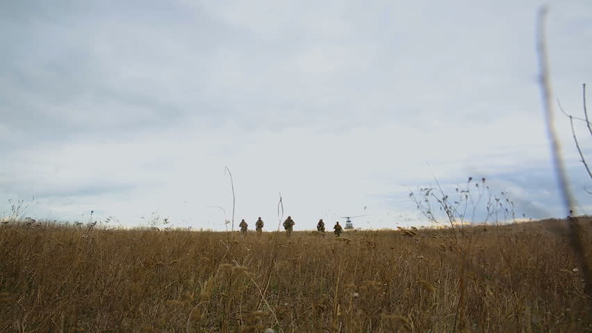 Helicopter flies over soldiers on battlefield. Soldiers fleeing a helicopter. Military exercises involving a helicopter in the field. Special force landing from helicopter. Bottom view.