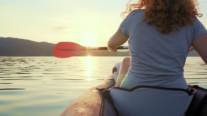 Happy young woman paddling on an inflatable kayak with her dog Jack Russell Terrier on water of large mountain lake beautiful orange sunset slow motion. Go Everywhere. Family Sports. Summer. Travel Royalty-Free Stock Footage #1018826386