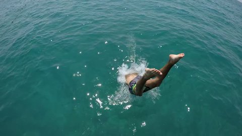  Over and underwater back view of a joung man in colored shorts diving hands first in sparkling green sea waters in summer in slow motion. 