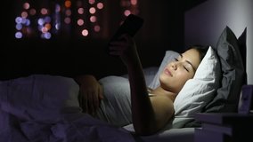 Surprised teen reading good news in a smart phone lying on a bed in the night at home