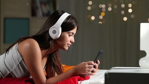 Profile of a happy teen listening to music relaxing on a bed in the night at home