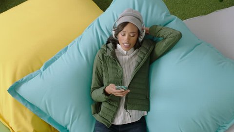 happy african american woman student using smartphone browsing online social media messages enjoying lunch break relaxing on colorful pillows listening to music in modern office top view