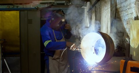 Attentive  African-american metalsmith using welding torch in workshop 4k
