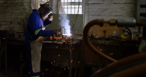 Attentive caucasian metalsmith using welding torch in workshop 4k