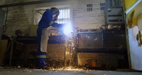 Attentive African-american metalsmith using welding torch in workshop 4k