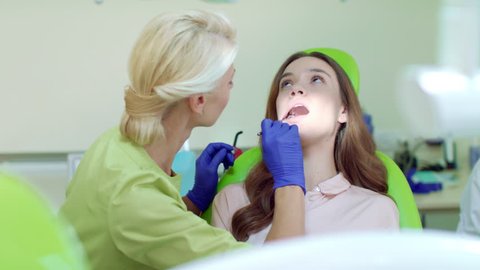 Regular dental checkup at professional dentist office. Happy woman on dental chair. Female dentist examining patient teeth with mouth mirror. Woman dentist with thumb up gesture