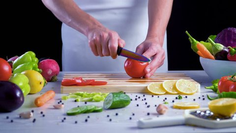 Chef is cutting vegetables in the kitchen, slicing tomato
