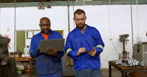 Two diverse metalsmiths discussing over laptop in workshop 4k