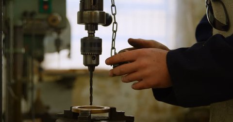Attentive Caucasian metalsmith using drill press machine in workshop 4k
