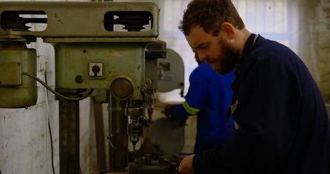 Attentive Caucasian metalsmith using drill press machine in workshop 4k