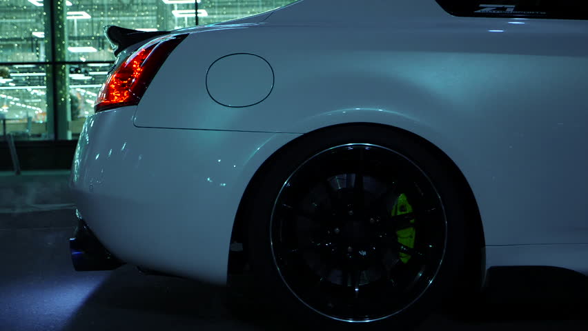 Luxury white sports car burns rubber off its tires. Makes Burnout with smoke on the night city background. Slow motion 