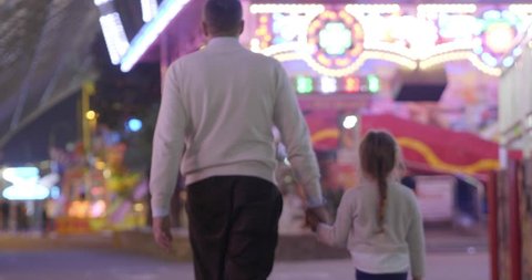 Portrait of a young father hand in hand with her daughter and taking her to the Luna Park. Concept: Happiness, freedom, fun.