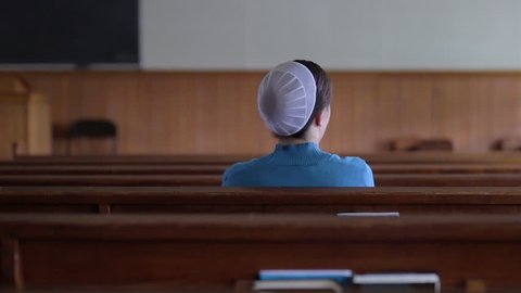 A young Mennonite woman sits in the pews of an empty church.