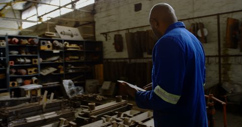 African-american metalsmith maintaining stocks on digital tablet in workshop 4k