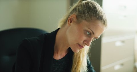 Focused business woman works at white desk in modern office during the daytime. Medium shot on 4K RED camera on a gimbal tracking backwards.