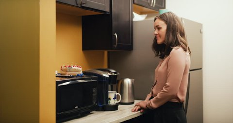 Content office worker makes coffee in office kitchen with cake on microwave. Dolly out shot on 4K RED camera on a gimbal.
