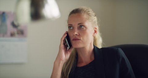 Blonde business woman talks on cell phone in office during the daytime. Medium to closeup shot on 4K RED camera.