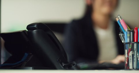 Receptionist answers phone in foreground in office during the daytime. Medium to closeup shot on 4K RED camera on a gimbal.