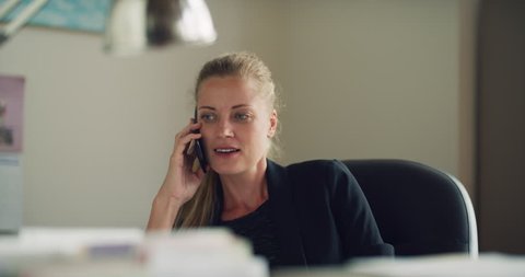 Friendly business woman talks on cell phone in office during the daytime. Medium to closeup shot on 4K RED camera on a gimbal.