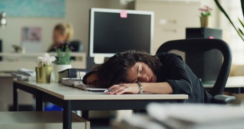 Exhausted business woman sleeping at her desk while working on a stack of papers during the daytime. Medium to closeup shot on 4K RED camera on a gimbal.