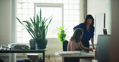 Two professional women work together at a computer in industrial office during the daytime. Wide to medium shot on 4K RED on a gimbal.