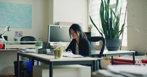 Contemplative female Asian business woman working hard in office during the daytime. Medium shot on 4K RED on a gimbal.