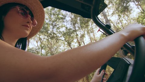 Beautiful woman wearing a hat and sunglasses driving an ATV through a forest in Australia, bright natural lighting. Medium close up shot on 4k RED camera.