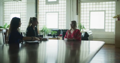 Business woman gets fired while sitting at big board room table in hipster industrial office during the daytime. Wide to medium shot on 4K RED on a gimbal.