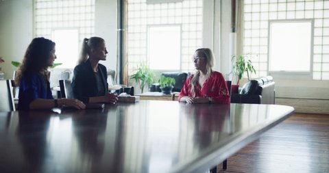 Business woman in red sits down and gets fired at meeting with her bosses at a big board room table in hipster industrial office during the daytime. Wide to medium shot on 4K RED on a gimbal.