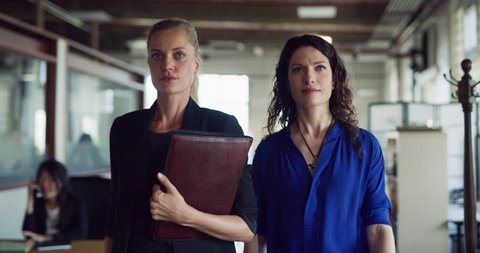 Two powerful business women walk down hallway in hipster industrial office during the daytime. Wide to medium shot on 4K RED on a gimbal.