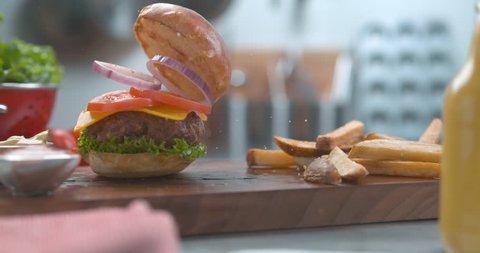 Bouncy hamburger and fries falling onto a wooden board on a table with bright studio lighting. Close up slow motion shot on 4k phantom fles camera. 