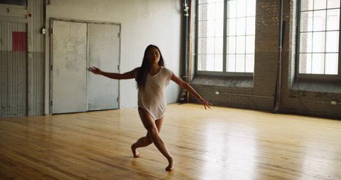 Beautiful asian dancer in industrial wood and brick windowed loft dances during daytime. Wide to long shot on 4K RED camera.