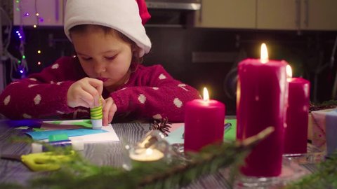 Pan shot. Children handicraft. Little girl glues New Year card. Table with Christmas decorations. French text on a sweater - falls