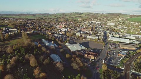 Aerial footage over the town of Bathgate in West Lothian, Scotland. Flying left. Passenger train arriving at Bathgate railway station
