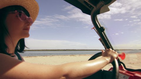 Beautiful woman wearing a hat and sunglasses driving an ATV along the beach in Australia, bright natural lighting. Medium shot on 4k RED camera.