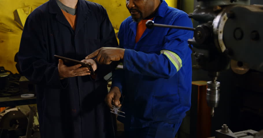 Close up of two diverse metalsmiths discussing over machine in workshop