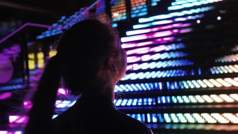 Young Beautiful Woman Standing Beside Neon RGB Lights, Nightlife. Young Woman Taking in the City at Night, Long Hair Side Profile Silhouetted 