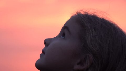 Kid looking up at the sky in nature. Little girl praying looking up at purple sky with hope, close-up. 
